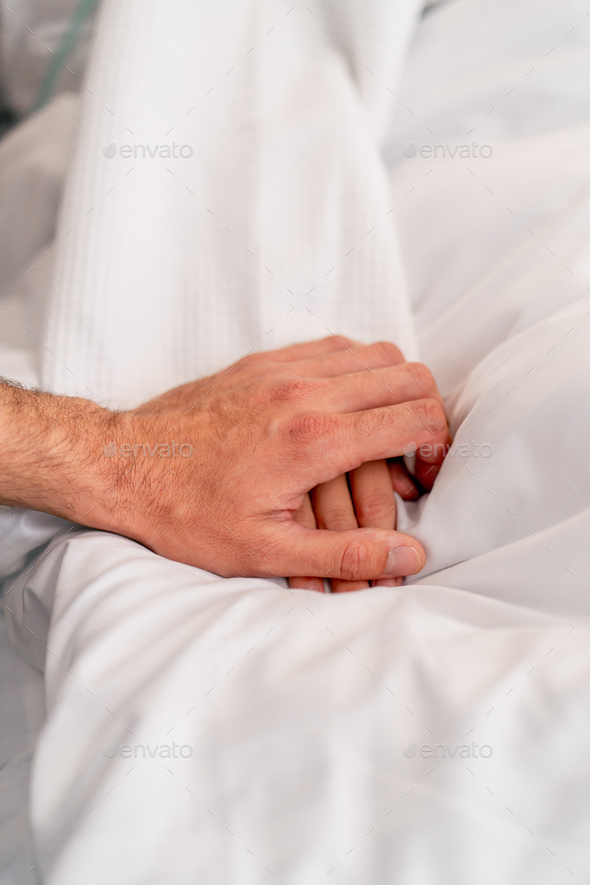 a male doctor's hand holding a female patient's hand on a bed in a hospital ward for moral support