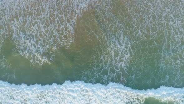 Horizontal Aerial Pan Looking Down Across Powerful Ocean Waves Breaking on The Sandy Beach