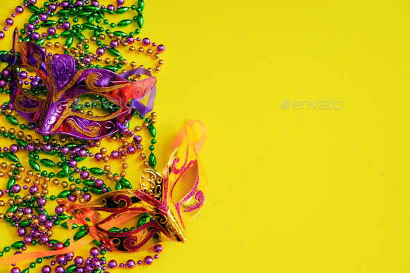 Two multi-colored carnival masks and beads on yellow background. Mardi Gras concept. Fat Tuesday.