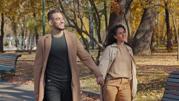 Young Hispanic Couple Walking in Autumn Park Guy and Girl Holding Hands Lovers Have Fun Chatting alt