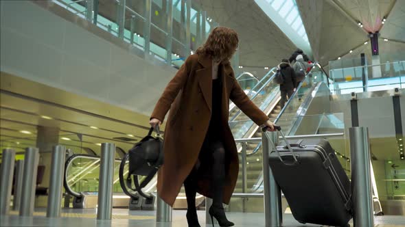 The Girl at the Airport is Late for the Plane and in a Hurry Leaves the Escalator and the Suitcase