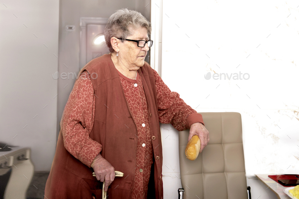 A sweet grandmother with a stick waits for eat with a loaf of bread at a nursing home, getting help.