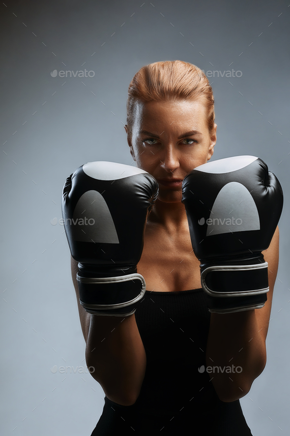 Beautiful woman with black boxing gloves on a gray background. Copy space, sport banner, hard work