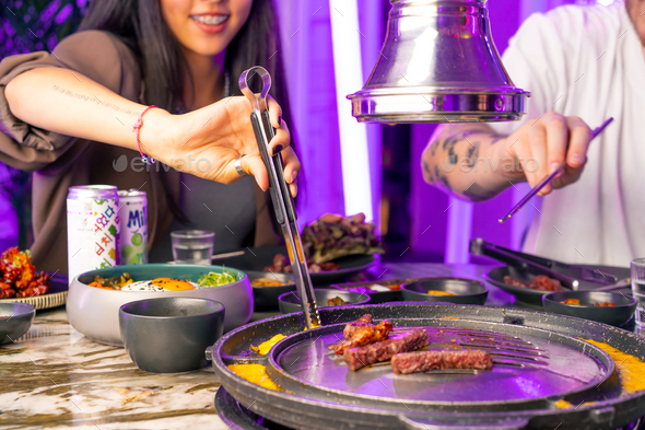 guests of a Korean restaurant take fried meat from grill with ...