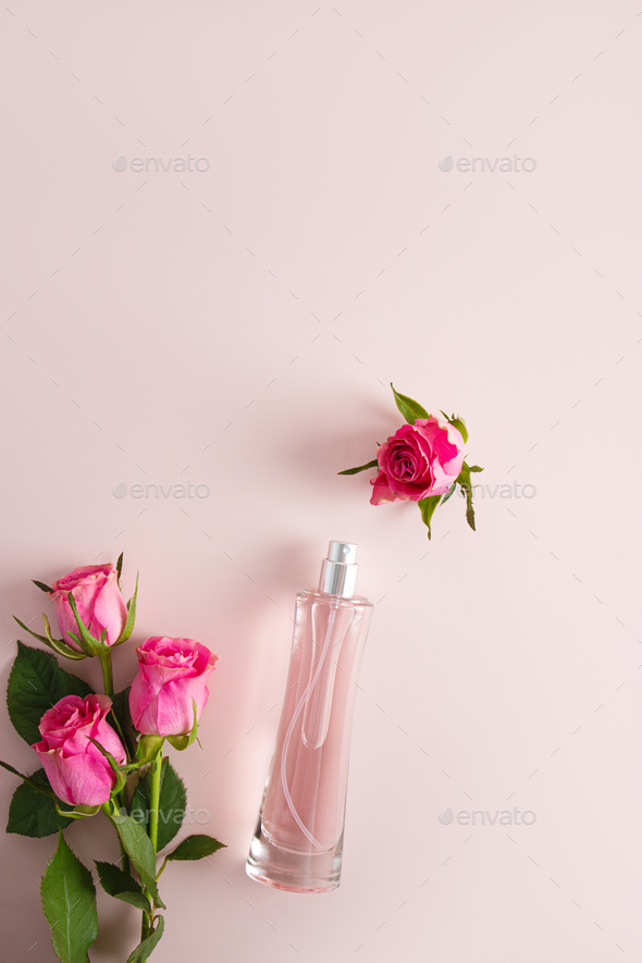 Elegant tall bottle of cosmetic spray or women's perfume on pink background with live roses.
