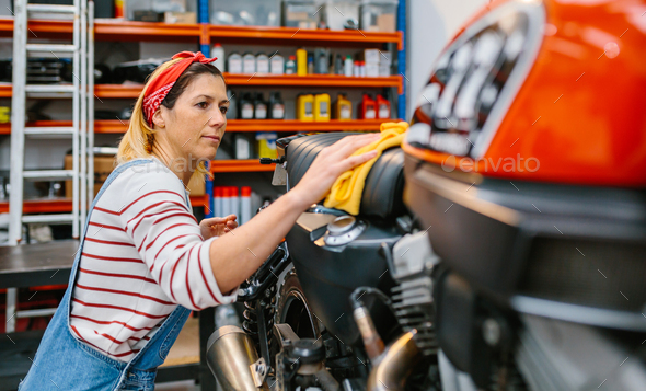 Mechanic woman cleaning motorcycle seat with cloth on factory