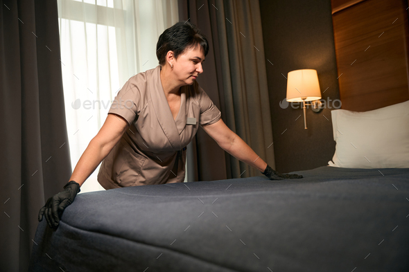 Maid involved in bed-making in hotel room in daytime