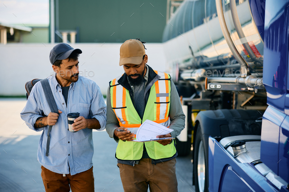 Black freight transportation manager and truck driver going through checklist on parking lot.