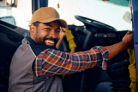 Happy black professional driver getting into his truck and looking at camera.