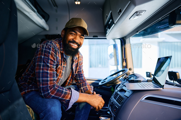 Happy black truck driver using laptop and looking at camera.