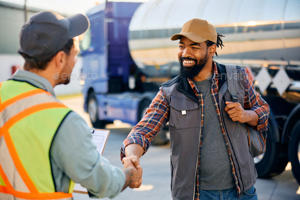 Happy black truck driver and freight transportation manager handshaking on a parking lot.