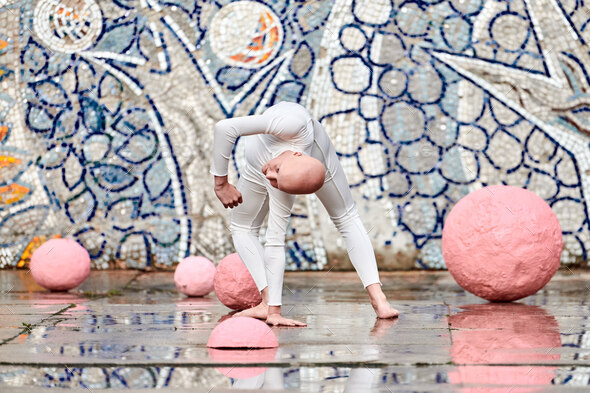 Outdoor dance of young ballerina girl with alopecia in white futuristic suit among pink spheres