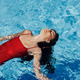 Happy woman swimming in pool in red swimsuit with loose long hair, skin  protection with sunscreen Stock Photo by shotprime