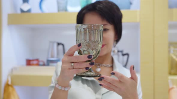 Brunette Woman Chooses a Glass in the Store Carefully Examines the Goods