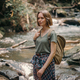 Attractive young female traveler with backpack standing by the mountain river and enjoying views - PhotoDune Item for Sale