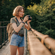 Smiling young female traveler photographing with camera while standing on the scenic bridge - PhotoDune Item for Sale