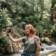 Happy young female traveler with backpack making selfie while standing by the mountain river - PhotoDune Item for Sale