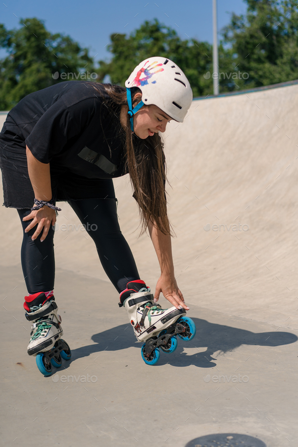 girl in protective helmet and roller skates tired after skating and stunts on ramp in skate park