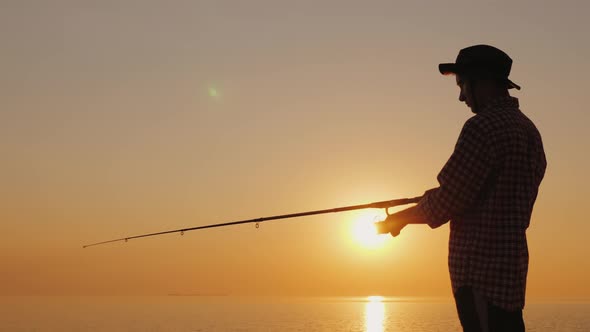 Silhouette of a Young Fisherman Fishing on the Beach at Sunset alt