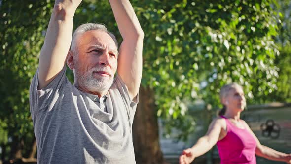 Elderly Man and Woman Raise Hands Up Practicing Yoga alt
