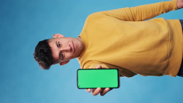 Man showing a smartphone with green screen while standing over an isolated background. alt