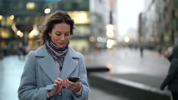 Charming Woman is Walking on Street and Viewing Social Nets in Smartphone Communicating Online alt