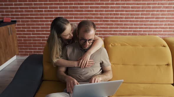 Freelancer Kissing Back the Cheek of Cheerful Woman Near Laptop alt