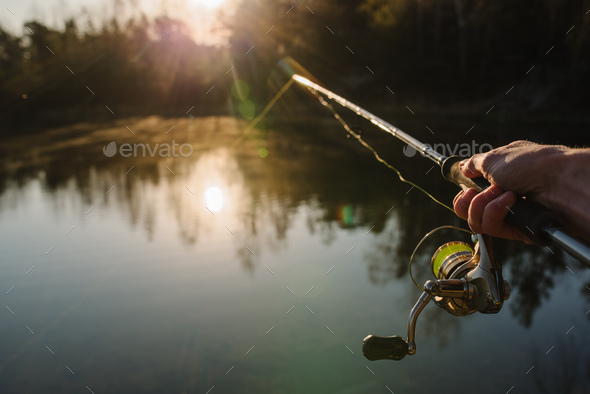 Fisherman with rod, spinning reel on the river bank. Sunrise