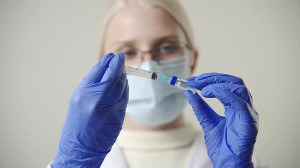 A Woman Doctor in a Medical Mask and Blue Gloves Draws a Blue Drug From a Glass Ampoule with a