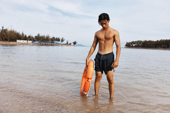 Guardian of Serenity: A Shirtless Asian lifeguard man in vibrant swimwear watches over beachgoers