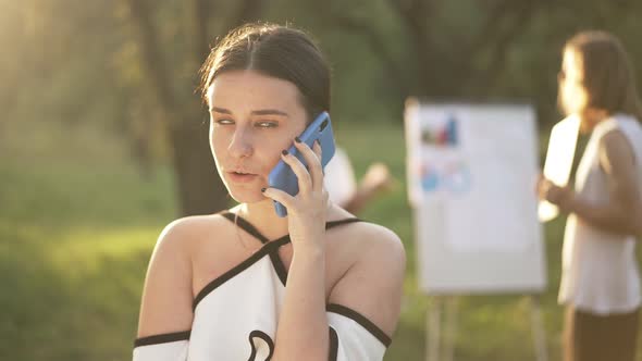 Bored Annoyed Beautiful Woman Talking on Phone Rolling Eyes Looking Back at Colleagues Discussing alt