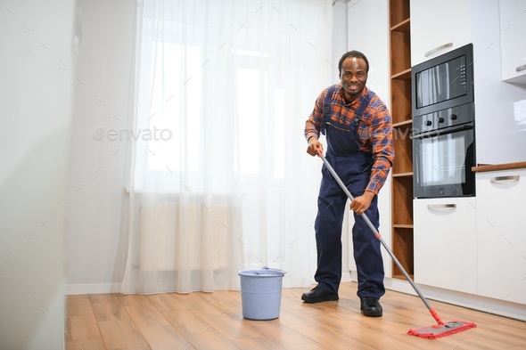 Young african man washes the floor with a mop in the room