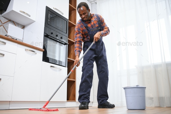 Young african man washes the floor with a mop in the room