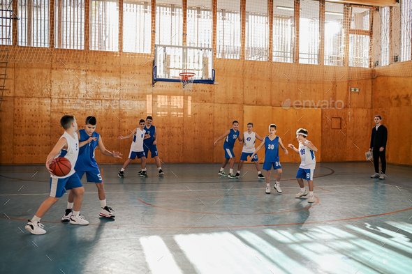 Junior basketball team practicing game on training with their coach at court.
