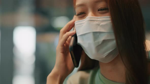 Young Beautiful Asian woman wearing a medical protective face mask talking on a smartphone alt