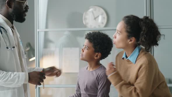 Black Pediatrician Examining Throat of Boy with Flashlight alt