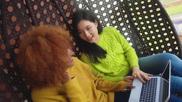 Two Young Women Sharing the Headphones and Listening To the Music From the Laptop. Multiracial alt