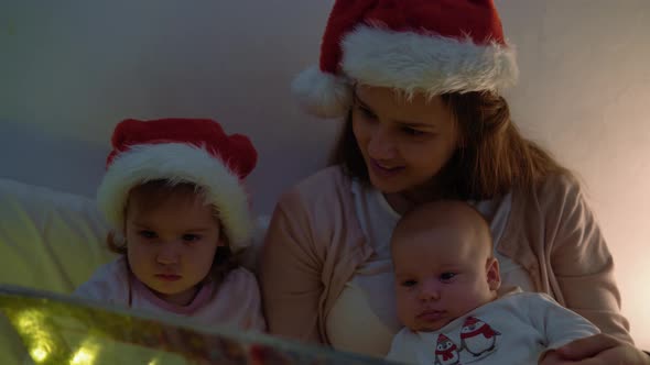 Happy Family Mother in Red Santa Hat Two Children Babies Little Baby Siblings Christmas Night in Bed