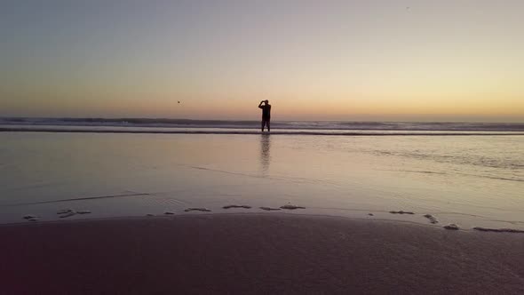 Silhouette of a Man Walking Along the Ocean at Sunset