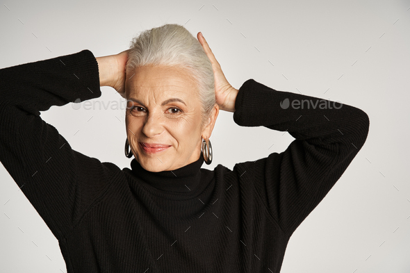 portrait of happy middle aged business woman in elegant attire and hoop earrings on grey background
