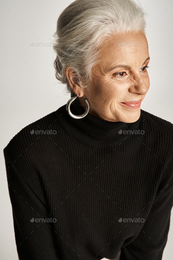 portrait of cheerful middle aged business woman in elegant attire and hoop earrings on grey backdrop