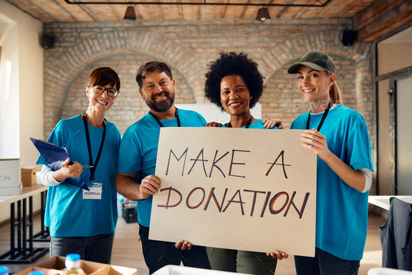 Multiracial group of happy volunteers with \'make a donation\' placard looking at camera.