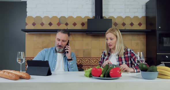 Woman Cutting Cucumber for Vegetable Salad while Her Handsome Husband Talking on Phone alt