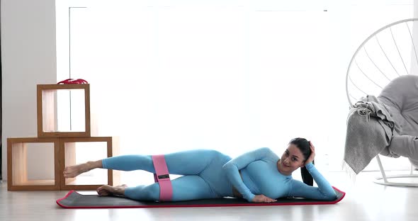 Resistance band fitness girl in sportswear doing leg workout floor exercises. alt