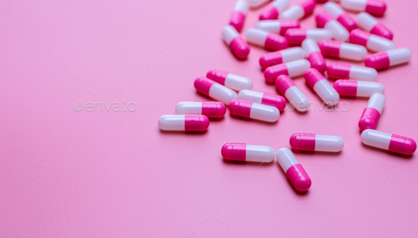 Pink and white antibiotic capsule pills spread on pink background. Antibiotic drug resistance.