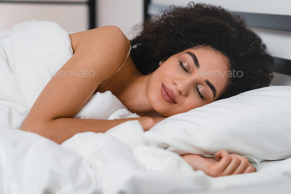 Coziness and comfort. African young woman sleeping on the white orthopedic mattress and bed linen