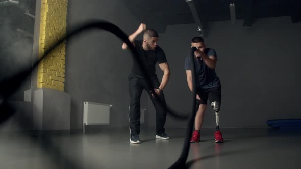 Young Man with Instructor Using Battle Ropes in Gym