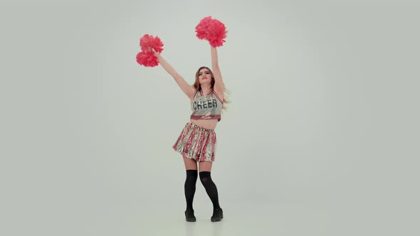 Young Cheerleader with Red Pompoms in Uniform is Dancing on White Background in Studio alt