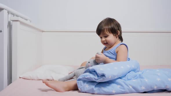 Child Is Sitting on the Bed in a T-shirt and Playing alt