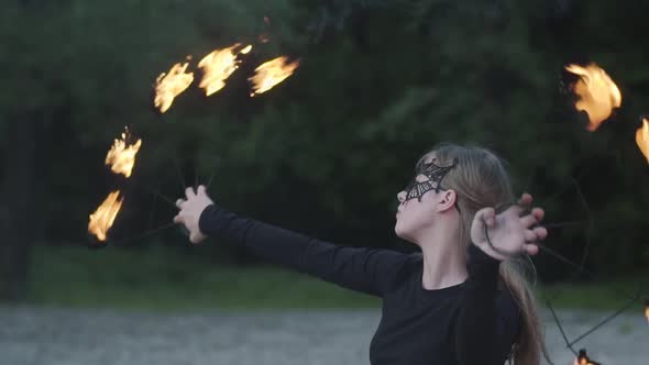 Portrait of Young Beautiful Woman in Mask Performing a Show with Flame in Front of Trees alt